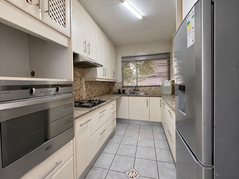 A functional galley-style kitchen featuring built-in cabinetry, a gas hob, an integrated oven, tiled backsplash, and durable tiled flooring.