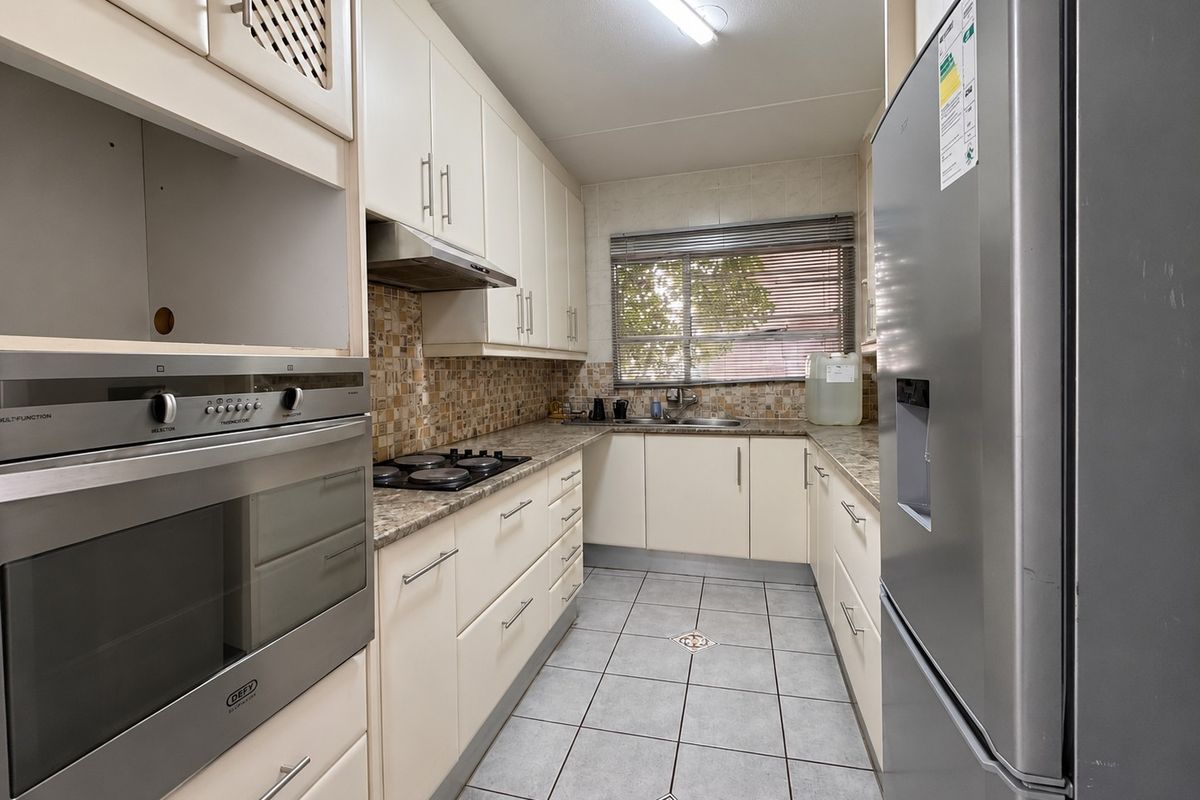 A functional galley-style kitchen featuring built-in cabinetry, a gas hob, an integrated oven, tiled backsplash, and durable tiled flooring.