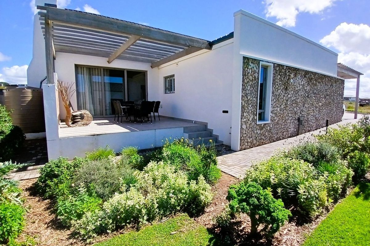 Rear view of the property featuring a raised timber deck with a pergola, stone-clad exterior wall, and a landscaped garden with a paved walkway.
