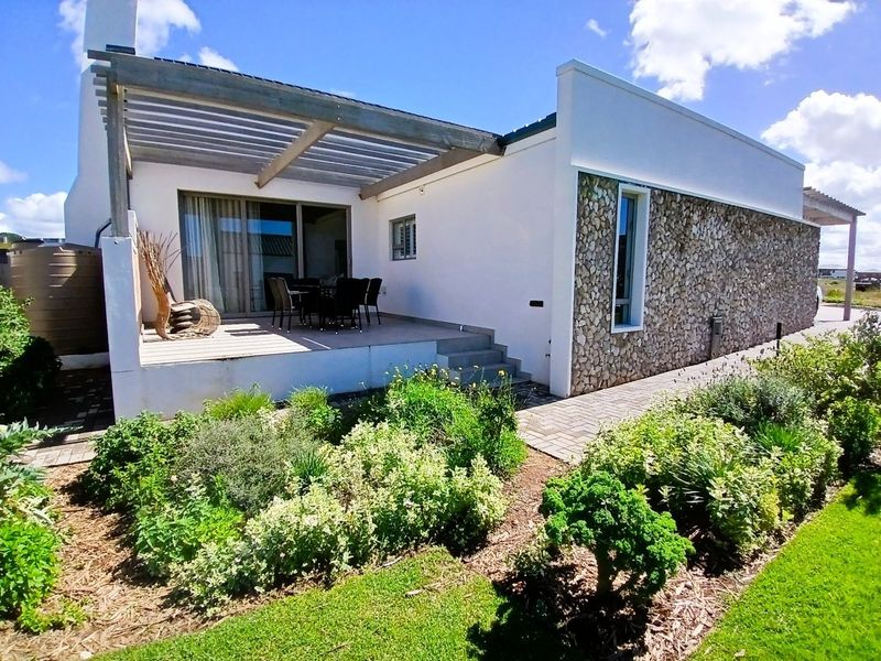 Rear view of the property featuring a raised timber deck with a pergola, stone-clad exterior wall, and a landscaped garden with a paved walkway.