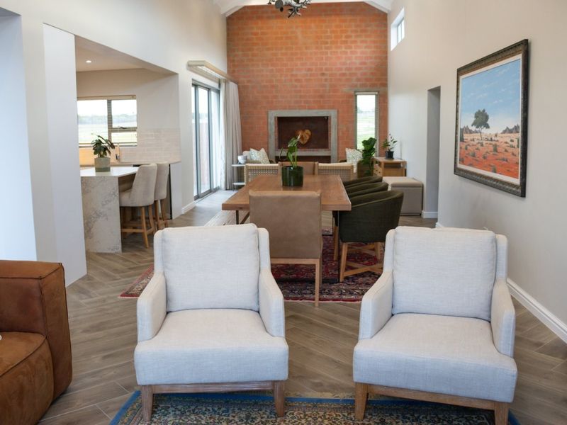 Spacious open-plan living and dining area featuring a striking exposed brick fireplace, vaulted ceilings, and a modern kitchen with a stone-topped island.