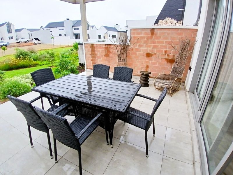 A covered patio area featuring tiled flooring and an exposed brick feature wall, providing direct access to the garden through sliding glass doors.