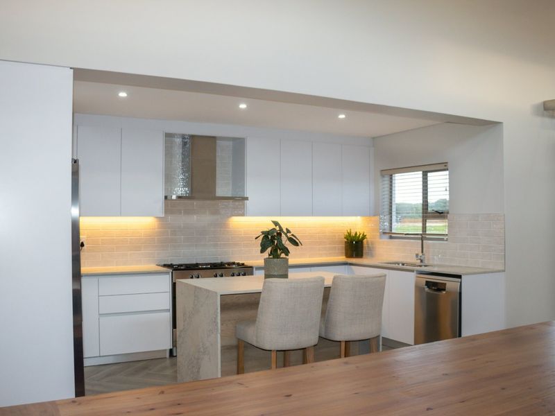 Modern kitchen featuring sleek white cabinetry, stone countertops, subway tile backsplash, integrated appliances, and warm under-cabinet lighting.