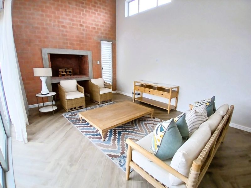 Spacious living room featuring a striking exposed brick wall, a built-in fireplace, high ceilings with clerestory windows, and modern herringbone flooring.