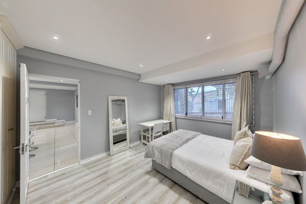 A well-maintained bedroom featuring modern laminate flooring, recessed downlighting, and an integrated air conditioning unit.