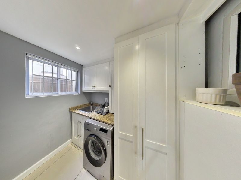 Compact laundry area featuring built-in white cabinetry, granite countertops, a stainless steel sink, and tiled flooring.