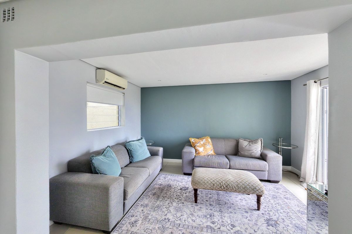 A well-maintained living room featuring tiled flooring, recessed downlighting, and a wall-mounted split-system air conditioning unit.