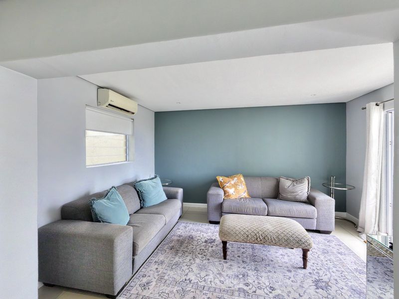 A well-maintained living room featuring tiled flooring, recessed downlighting, and a wall-mounted split-system air conditioning unit.