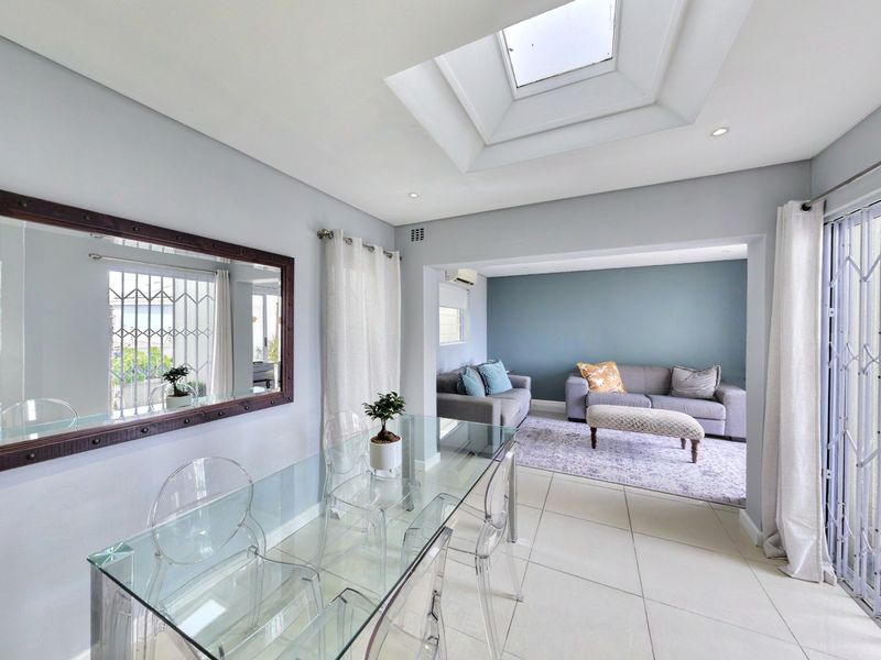 Bright open-plan living and dining area featuring a large skylight, neutral tiled flooring, and direct access to an outdoor space via security gates.