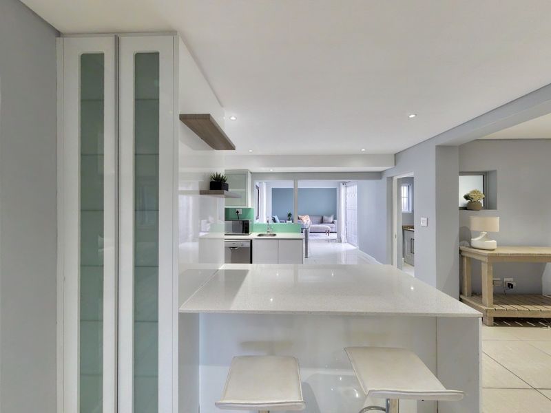 Modern open-plan kitchen featuring sleek white cabinetry, quartz countertops, and a breakfast bar, seamlessly flowing into the adjacent living area.