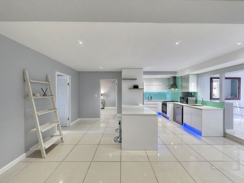 Modern open-plan kitchen featuring a central island, sleek white cabinetry, glass splashbacks, and integrated appliances, flowing into a bright, tiled living area.