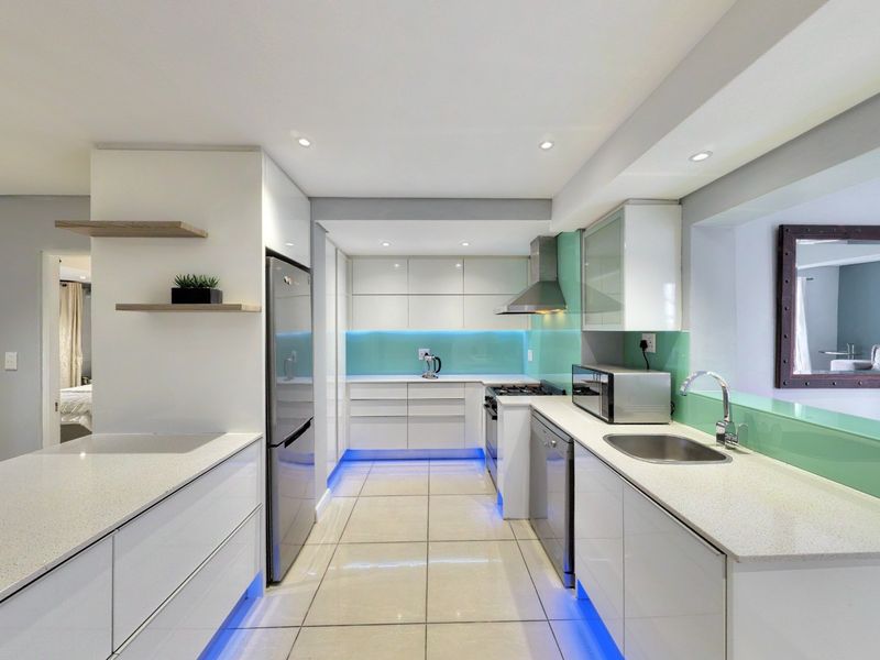 Modern kitchen featuring sleek white cabinetry, stone countertops, glass splashbacks, integrated lighting, and high-quality stainless steel appliances.
