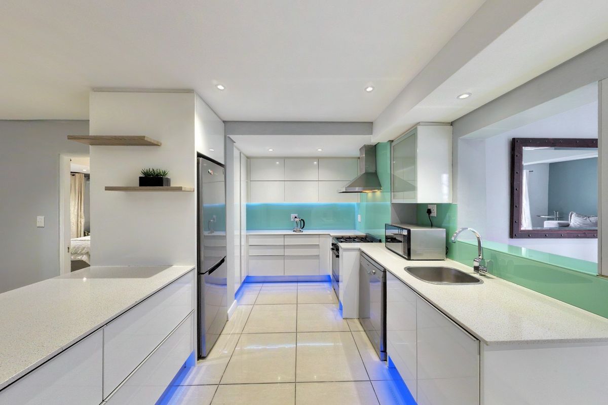 Modern kitchen featuring sleek white cabinetry, stone countertops, glass splashbacks, integrated lighting, and high-quality stainless steel appliances.
