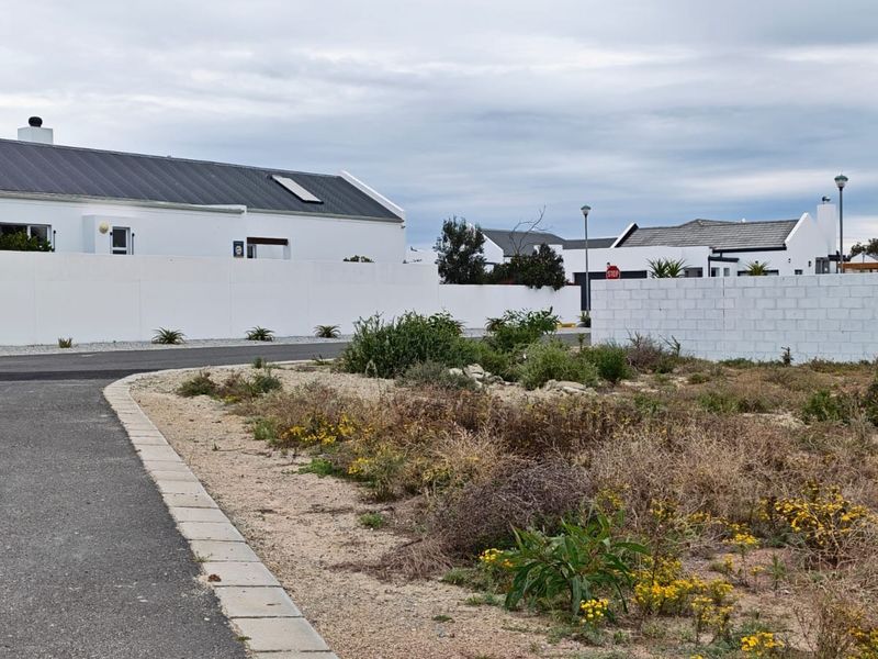 A street-level view of a vacant residential plot featuring established boundary walls, paved road access, and surrounding residential development.