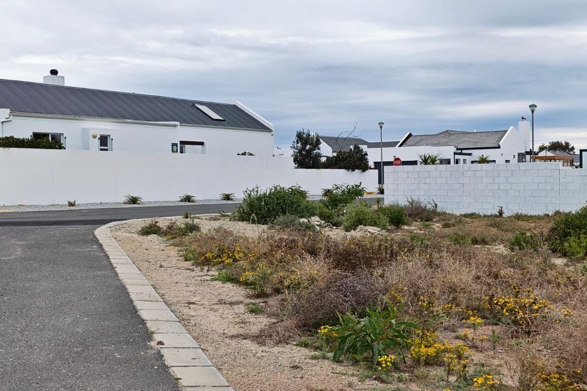 A street-level view of a vacant residential plot featuring established boundary walls, paved road access, and surrounding residential development.