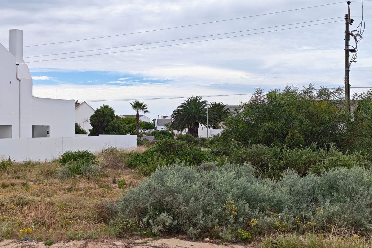 A vacant residential plot featuring natural vegetation, a boundary wall, and nearby utility infrastructure in a developed residential area.