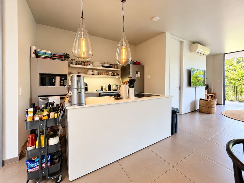 Modern open-plan kitchen and living area featuring a central island, sleek cabinetry, tiled flooring, and direct access to a balcony.