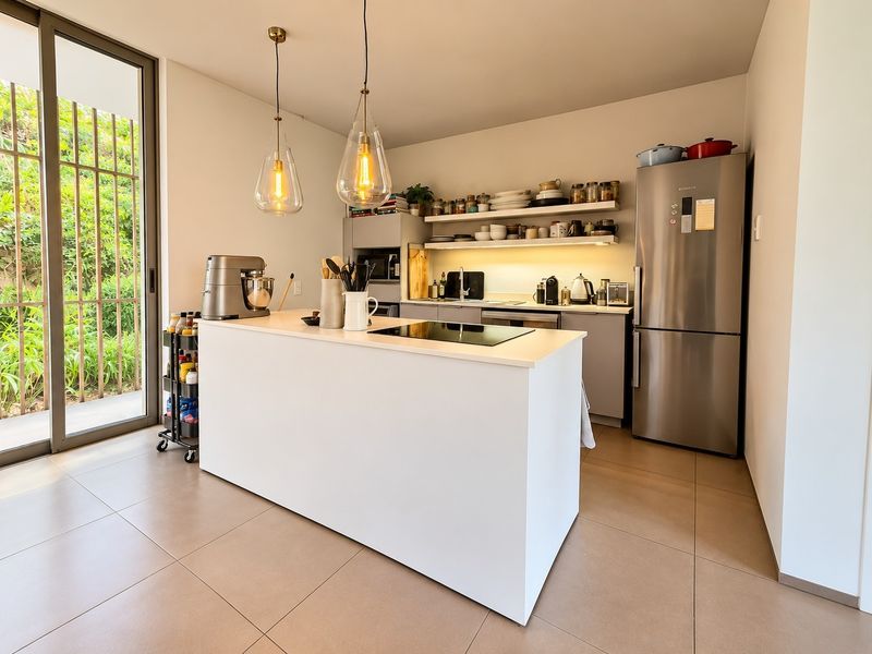 Modern kitchen featuring a central island, sleek cabinetry, open shelving, and direct access to an outdoor area through large sliding glass doors.