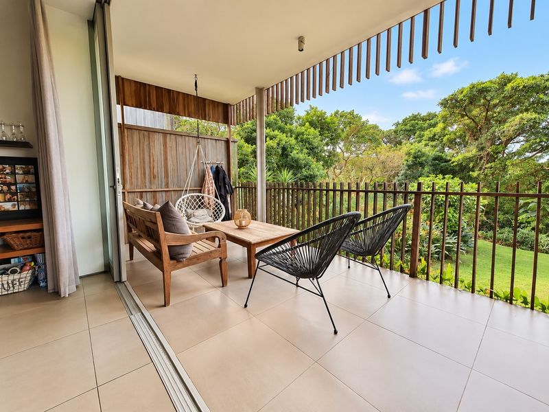A spacious covered balcony featuring tiled flooring, timber privacy screening, and a timber balustrade, offering a pleasant outlook over the surrounding greenery.