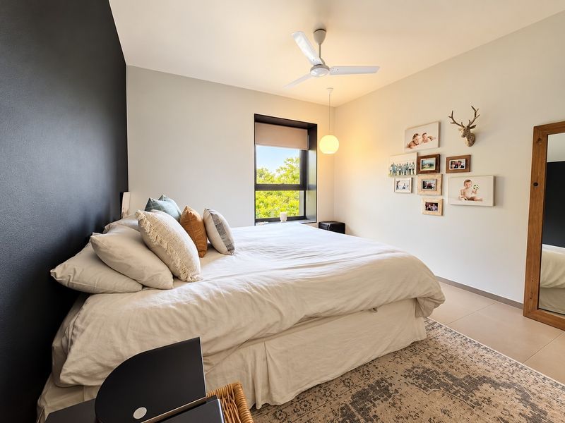 A well-maintained bedroom featuring a modern ceiling fan, neutral tiled flooring, and a large window providing natural light and a pleasant outdoor view.