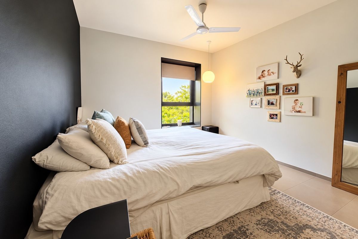 A well-maintained bedroom featuring a modern ceiling fan, neutral tiled flooring, and a large window providing natural light and a pleasant outdoor view.
