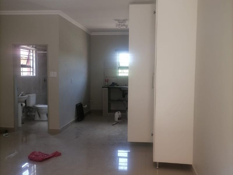 Open plan living area featuring tiled floors, built-in storage, and an unfinished kitchen area, with an adjacent bathroom visible.