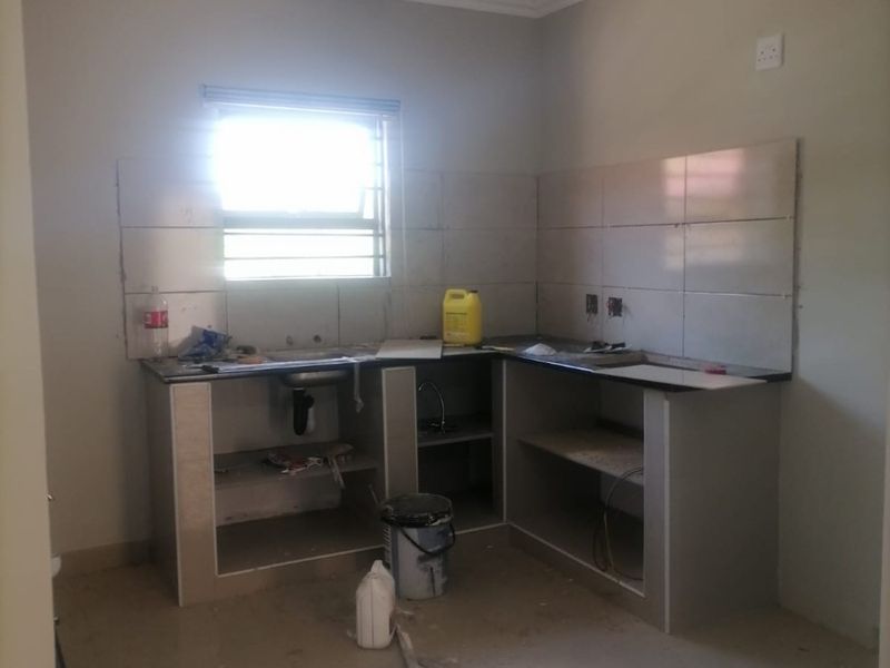 An unfinished kitchen area featuring tiled splashbacks, a built-in counter with a sink, and tiled flooring, currently undergoing renovation.