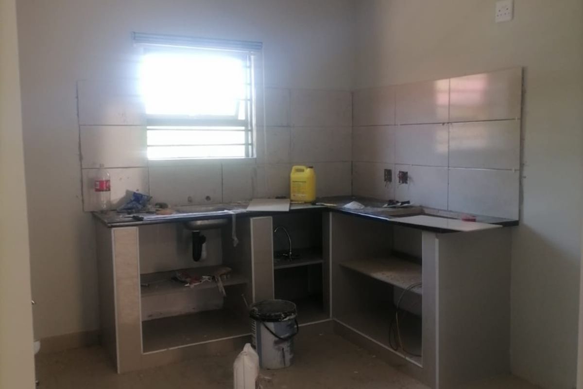 An unfinished kitchen area featuring tiled splashbacks, a built-in counter with a sink, and tiled flooring, currently undergoing renovation.