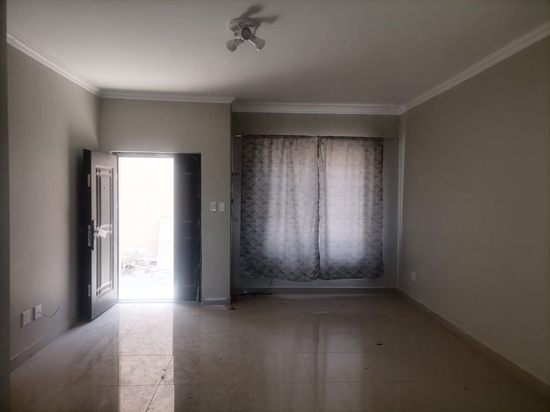An empty living room featuring tiled flooring, ceiling cornice, and a security entrance door, offering a neutral blank canvas for interior design.