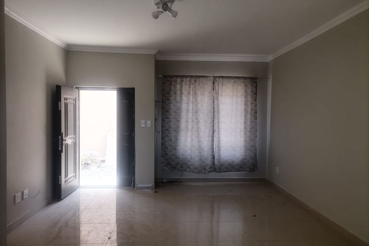 An empty living room featuring tiled flooring, ceiling cornice, and a security entrance door, offering a neutral blank canvas for interior design.