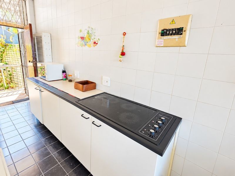 A functional kitchen featuring built-in cabinetry, an integrated electric cooktop, and tiled finishes, with direct access to an outdoor area.
