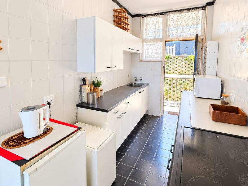 A functional galley-style kitchen featuring white cabinetry, dark countertops, ceramic tiling, and direct access to an outdoor area.