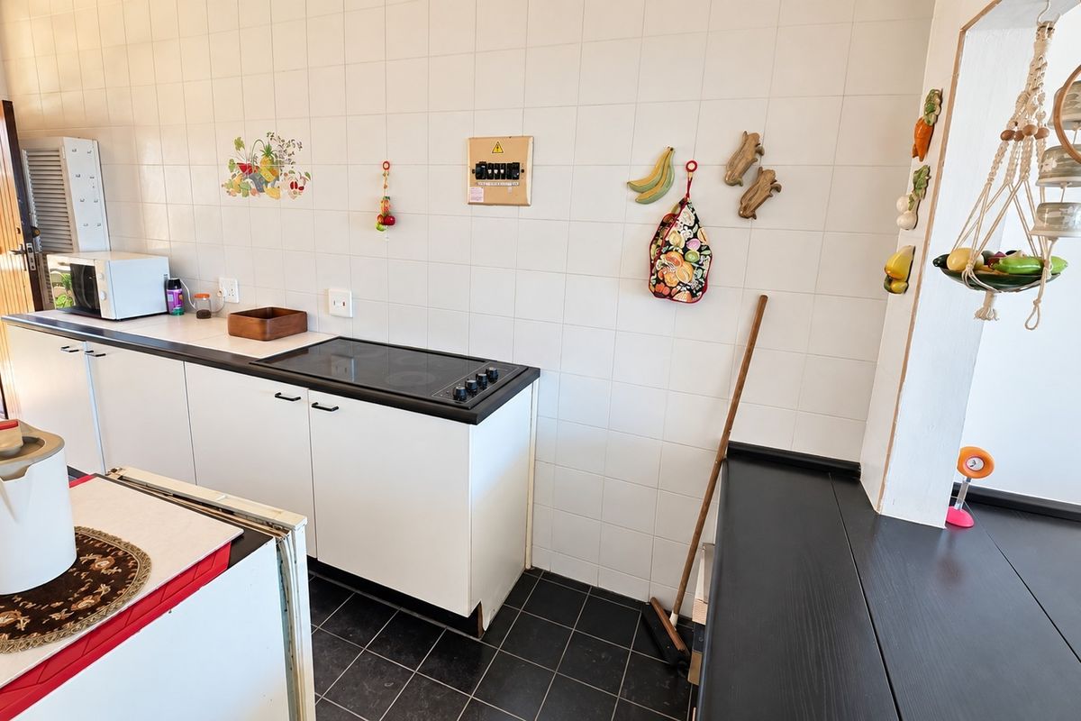 A functional kitchen featuring white cabinetry, a black countertop with an integrated electric hob, tiled wall splashbacks, and dark floor tiles.