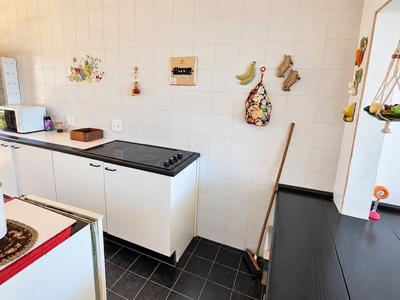 A functional kitchen featuring white cabinetry, a black countertop with an integrated electric hob, tiled wall splashbacks, and dark floor tiles.