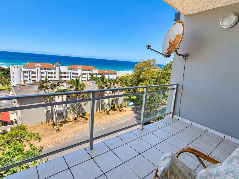 A balcony featuring tiled flooring and a glass balustrade, offering an elevated view of the surrounding neighborhood and the ocean.