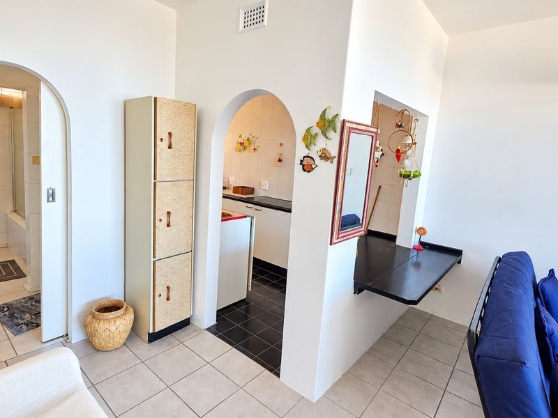 Open plan living area featuring arched doorways leading to a kitchen and bathroom, with tiled flooring and a built-in breakfast bar.