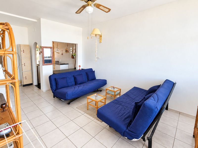 Open plan living area featuring tiled flooring, a ceiling fan, and a partial view into the adjacent kitchen space.
