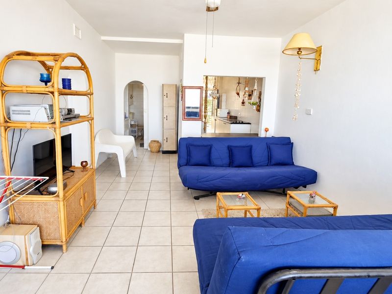 Open-plan living area featuring tiled flooring, an arched doorway, and a convenient pass-through window connecting to the kitchen space.