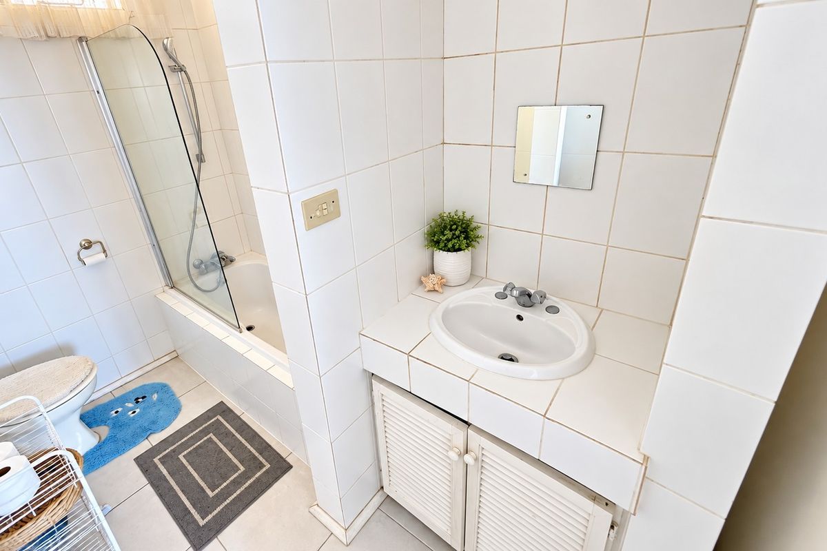 A functional bathroom featuring a tiled vanity with a drop-in basin, a built-in bathtub with a glass shower screen, and classic white wall tiling.