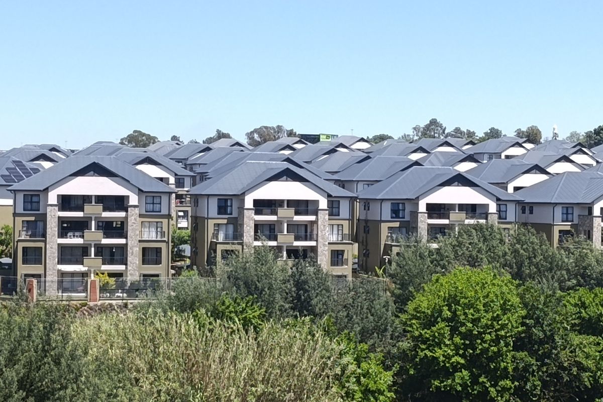 An elevated aerial view of a modern apartment complex featuring multiple residential buildings with pitched roofs, balconies, and stone facade detailing.