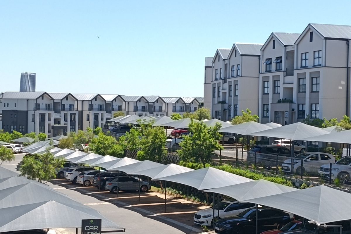 An elevated view of a modern apartment complex featuring multiple residential blocks, paved driveways, and extensive shade-cloth covered parking areas.