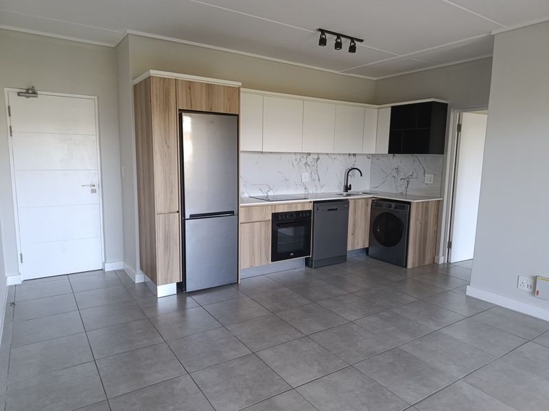 Modern open-plan kitchen featuring sleek wood-tone and white cabinetry, marble-look splashback, integrated appliances, and neutral tiled flooring in a well-maintained apartment space.