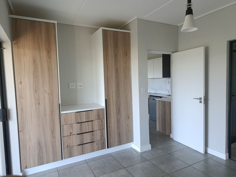 A bright living area featuring modern wood-finish built-in cabinetry, neutral tiled flooring, and a clean, contemporary aesthetic with direct access to the kitchen.