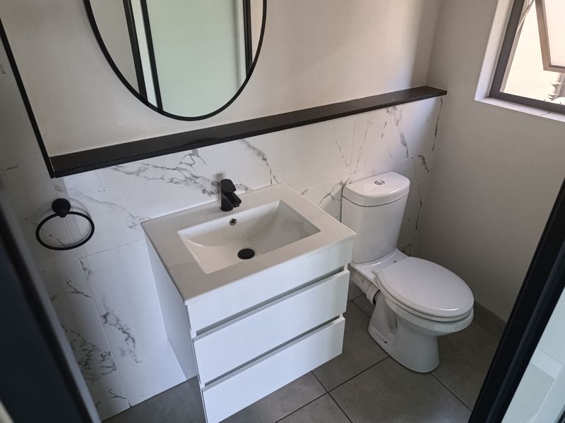 Modern bathroom featuring a sleek vanity cabinet with a ceramic basin, black fixtures, and elegant marble-look wall tiling.