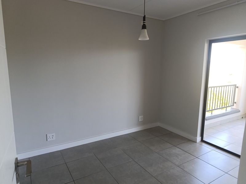 A bright, empty living area featuring neutral grey walls, tiled flooring, and direct access to a private balcony through a sliding glass door.
