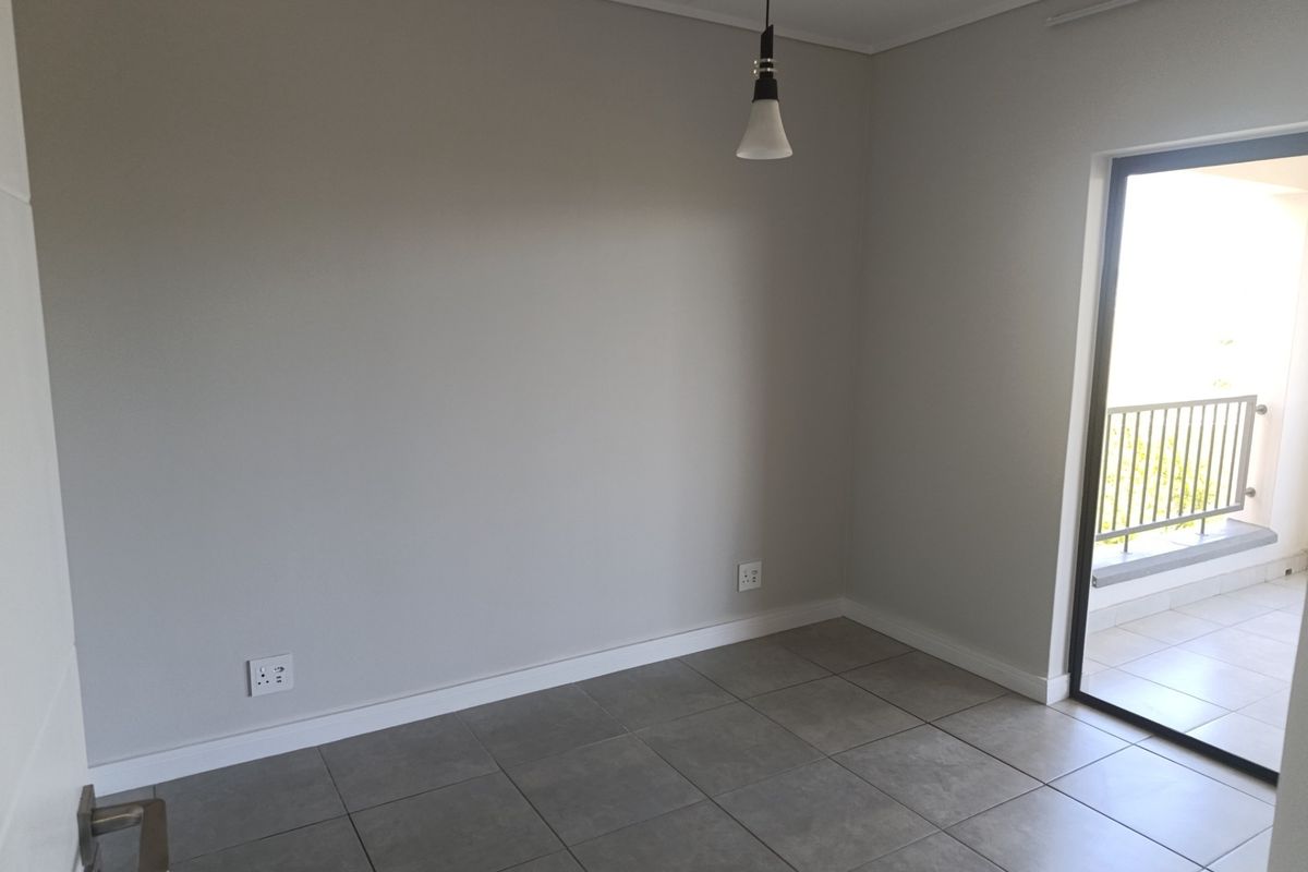 A bright, empty living area featuring neutral grey walls, tiled flooring, and direct access to a private balcony through a sliding glass door.