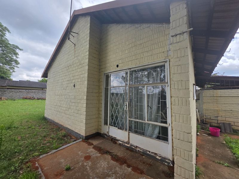Rear exterior view of the property featuring a painted brick facade, sliding glass door with security gate, and a concrete patio area.
