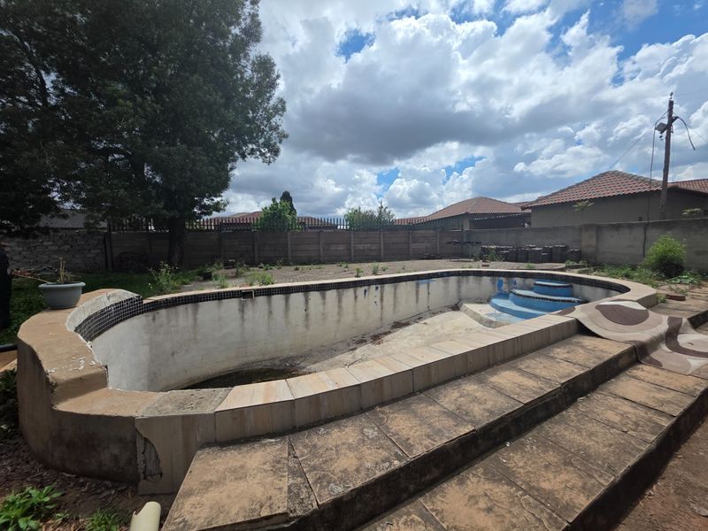 An outdoor swimming pool area featuring a concrete boundary wall and tiled coping, currently requiring significant maintenance and restoration of the pool shell and surroundings.