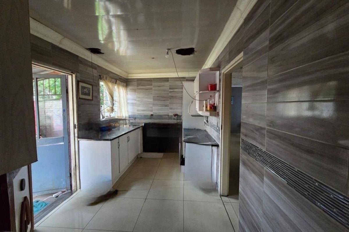 A kitchen space featuring tiled walls and floors with built-in cabinetry, currently requiring ceiling repairs and electrical fixture installation.