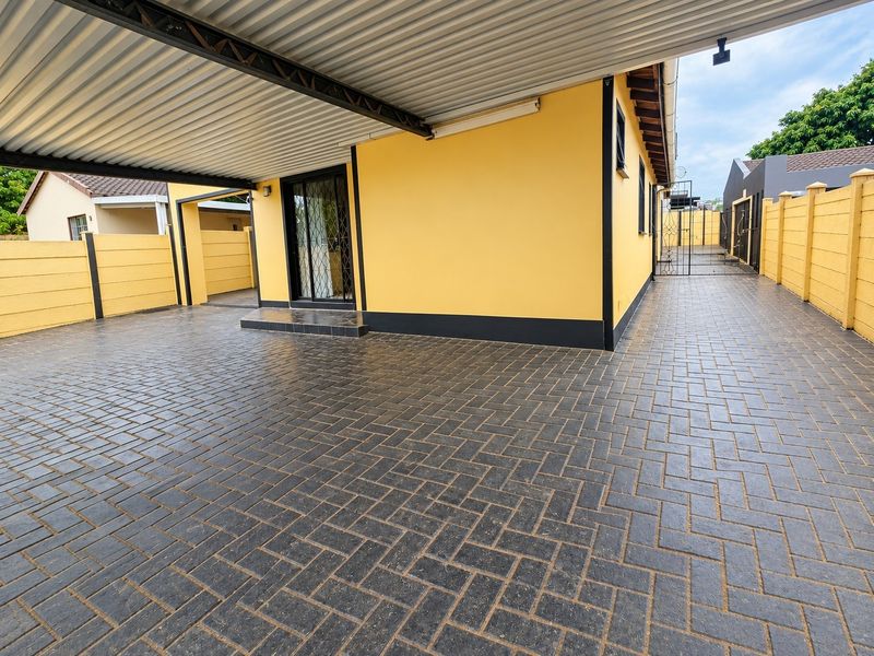 A well-maintained rear exterior area featuring a covered carport, extensive paved driveway, and secure perimeter walling with gated access.